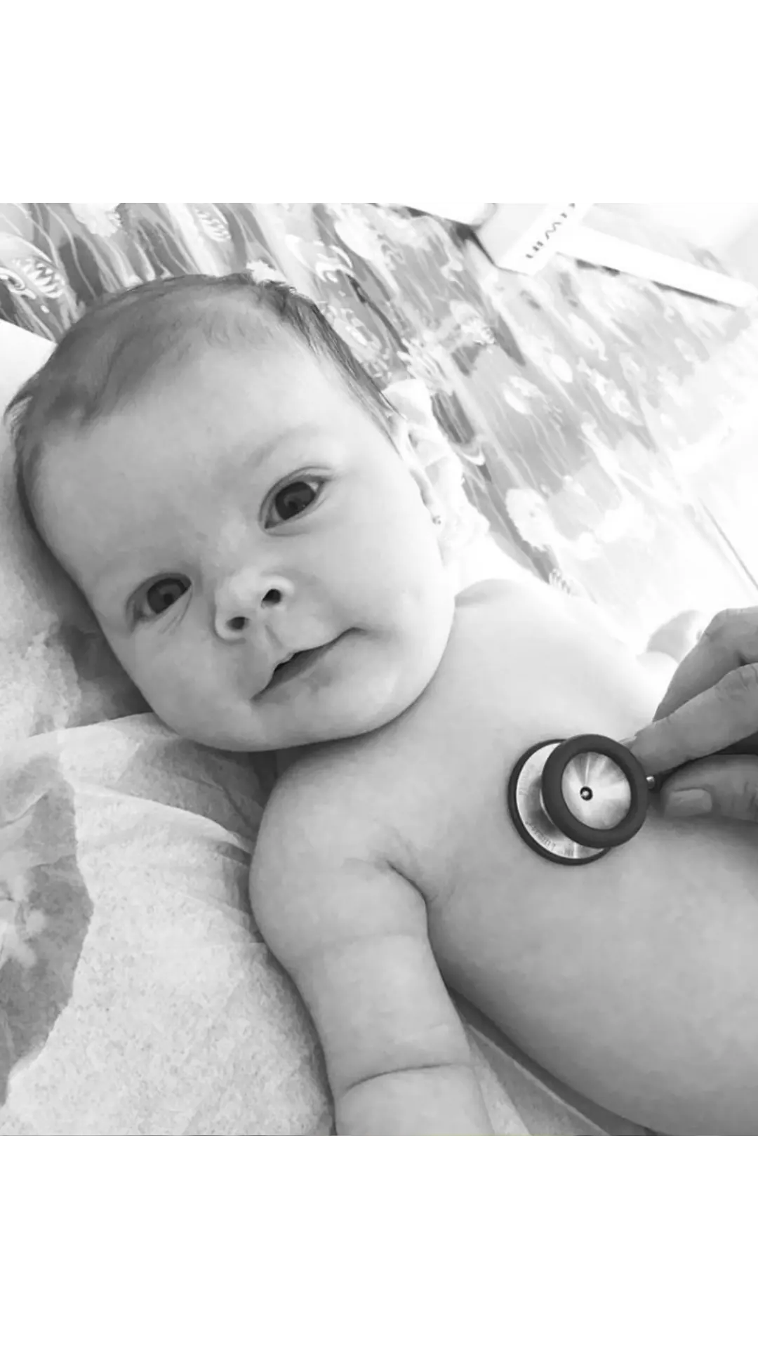 Bebê deitado durante a ausculta com estetoscópio, em foto preto e branco.