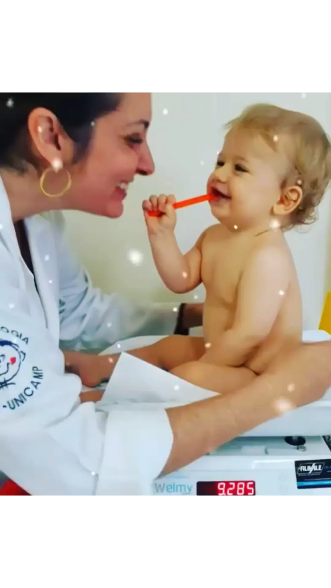 Dra. Sabrina Nunes sorrindo para um bebê durante a pesagem no consultório.